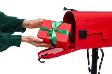 Woman putting Christmas gift into mailbox on white background, closeup. Sending present by mail