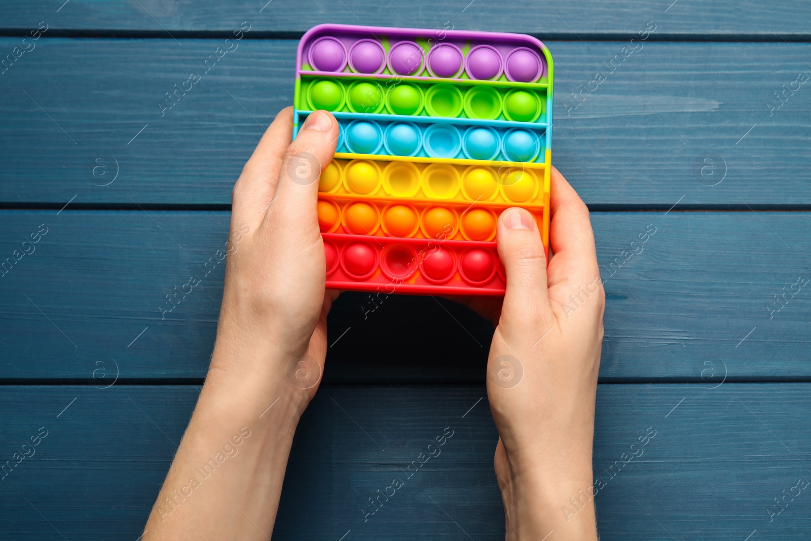 Photo of Woman using pop it fidget toy at blue wooden table, top view