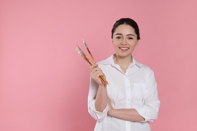 Photo of Woman with paintbrushes on pink background, space for text. Young artist