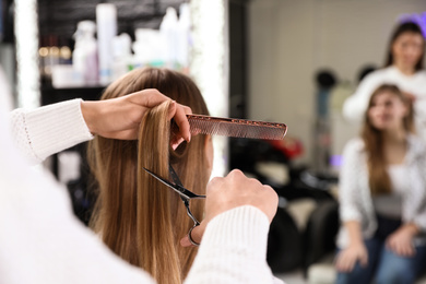 Photo of Hairdresser making stylish haircut with professional scissors in salon, closeup
