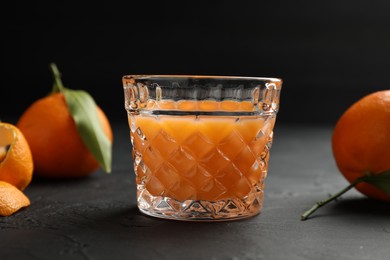 Tasty tangerine liqueur in glass and fresh fruits on black textured table, closeup