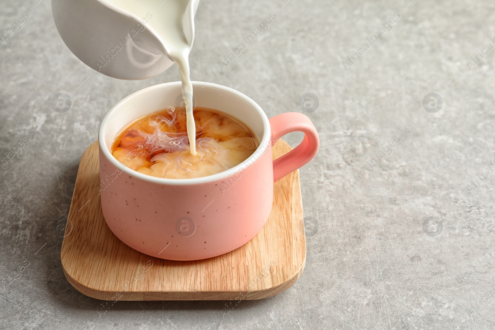 Photo of Pouring milk into cup of black tea on gray table