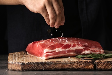Photo of Man salting fresh raw meat on wooden board, closeup