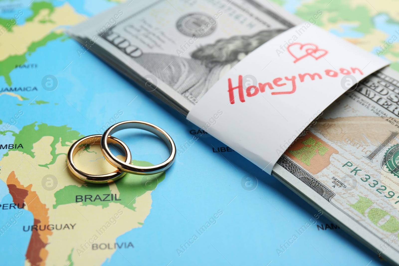 Photo of Two golden rings and stack of money with word Honeymoon on world map, closeup