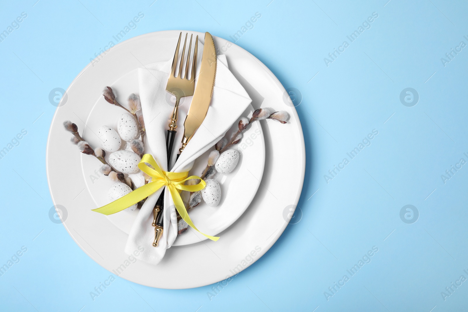 Photo of Festive table setting with willow twigs on light blue background, top view with space for text. Easter celebration