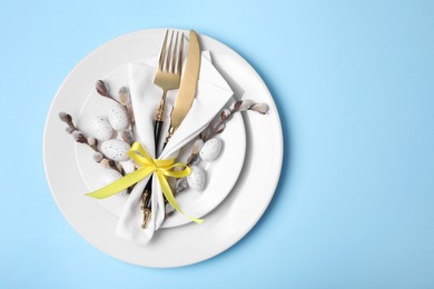 Photo of Festive table setting with willow twigs on light blue background, top view with space for text. Easter celebration