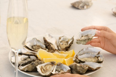 Photo of Woman holding fresh oyster over plate, focus on hand