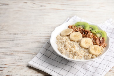 Photo of Bowl of quinoa porridge with walnuts, kiwi, banana and milk on white wooden background. Space for text
