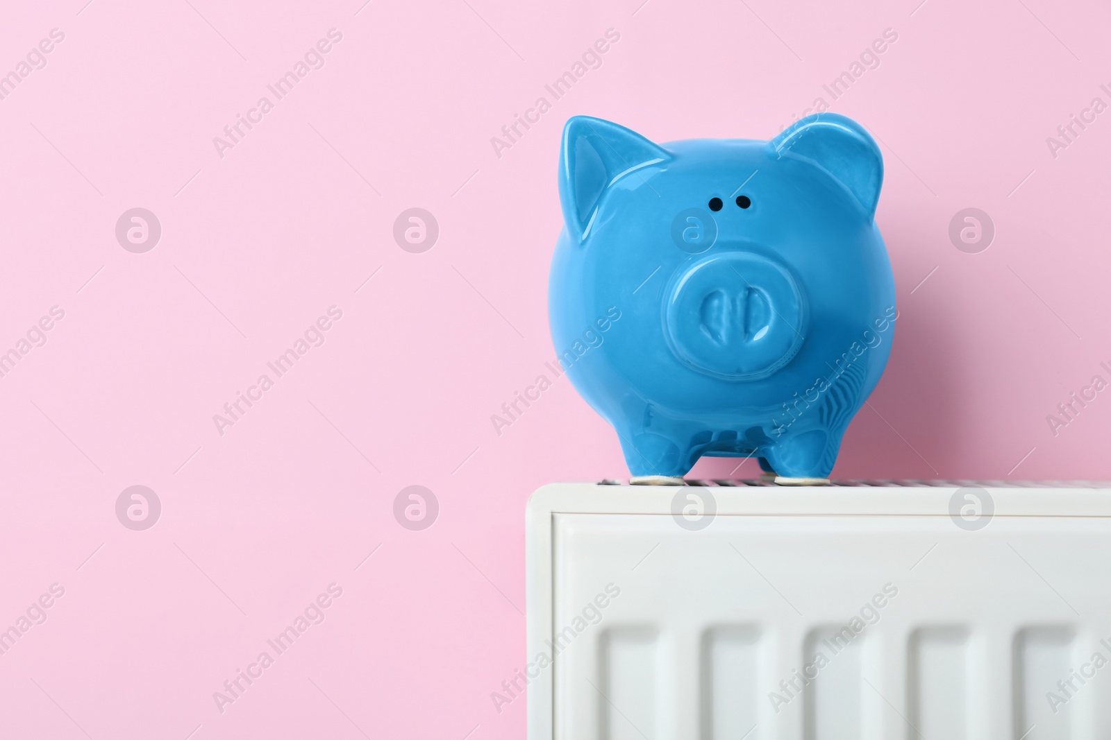 Photo of Piggy bank on heating radiator against pink background, space for text