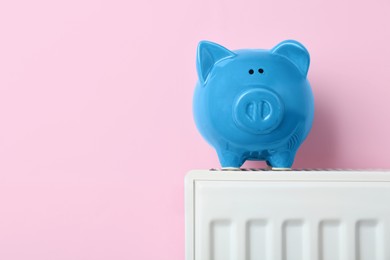 Photo of Piggy bank on heating radiator against pink background, space for text