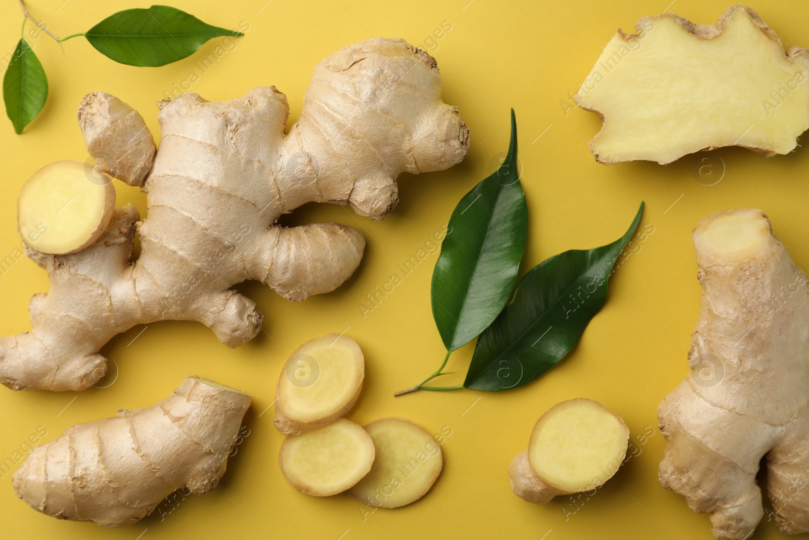 Photo of Fresh ginger with green leaves on pale light yellow background, flat lay