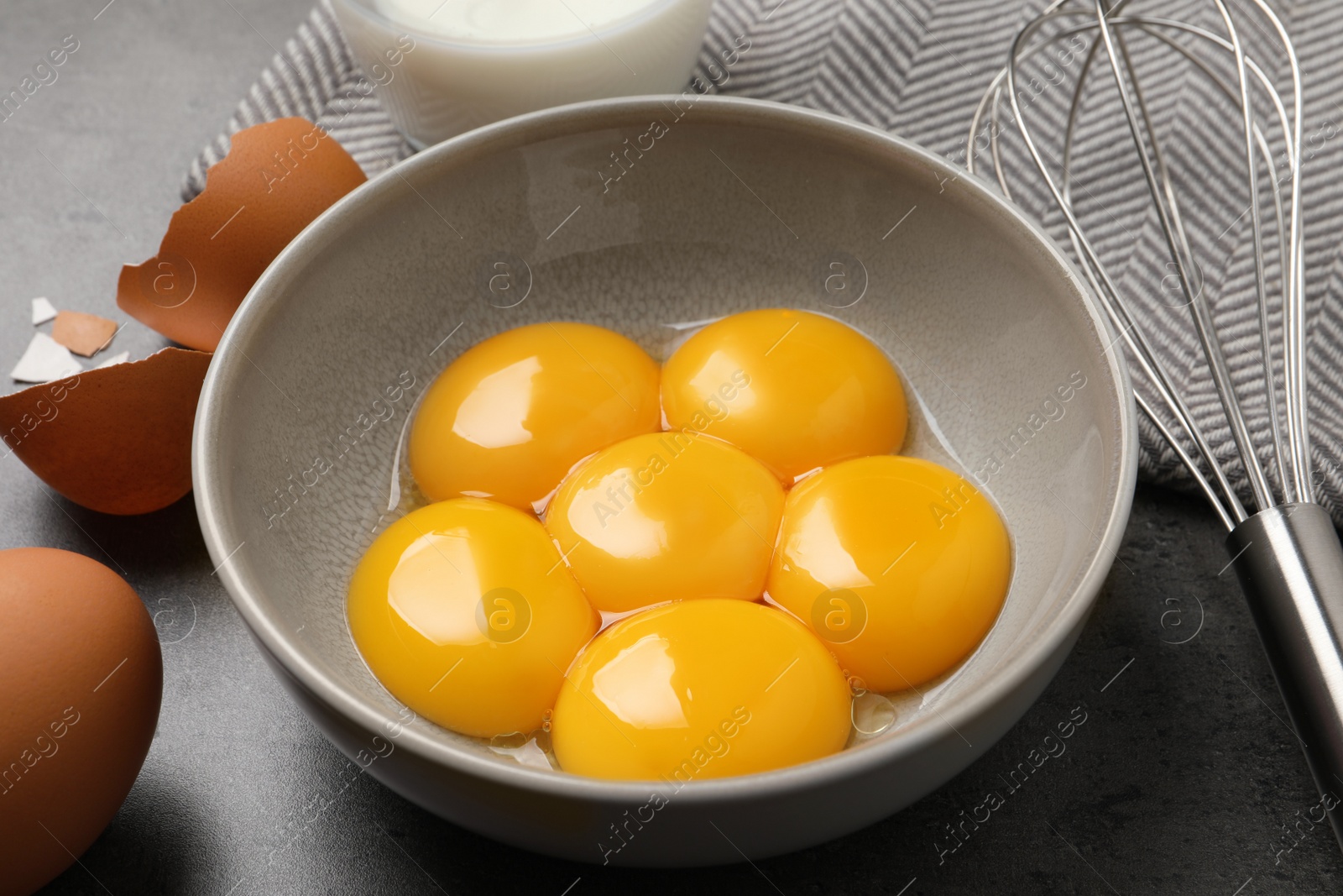 Photo of Bowl with raw egg yolks and whisk on grey table