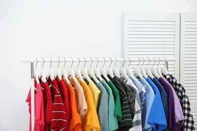 Photo of Rack with bright clothes in room. Rainbow colors