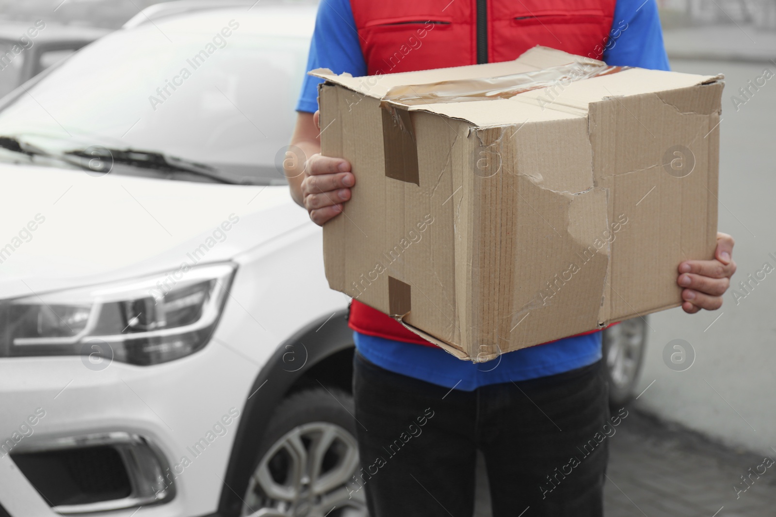 Photo of Courier with damaged cardboard box outdoors, closeup. Poor quality delivery service