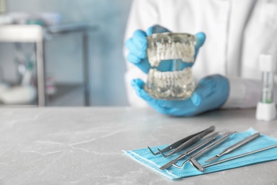 Dentist tools and blurred doctor with typodont teeth at table, closeup. Space for text