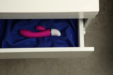 Pink vibrator in drawer indoors, above view. Sex toy