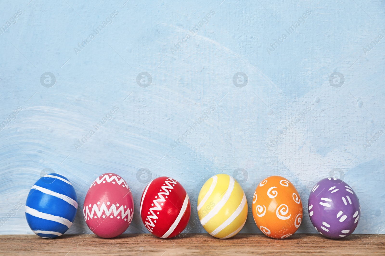 Photo of Decorated Easter eggs on table near color wall. Space for text