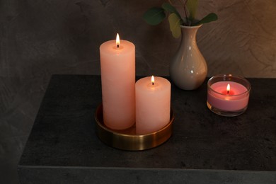 Scented candles near vase with eucalyptus branch on table in dark room