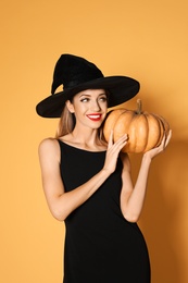 Photo of Beautiful woman wearing witch costume with pumpkin for Halloween party on yellow background