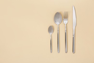 Photo of Stylish silver cutlery set on beige background, flat lay. Space for text