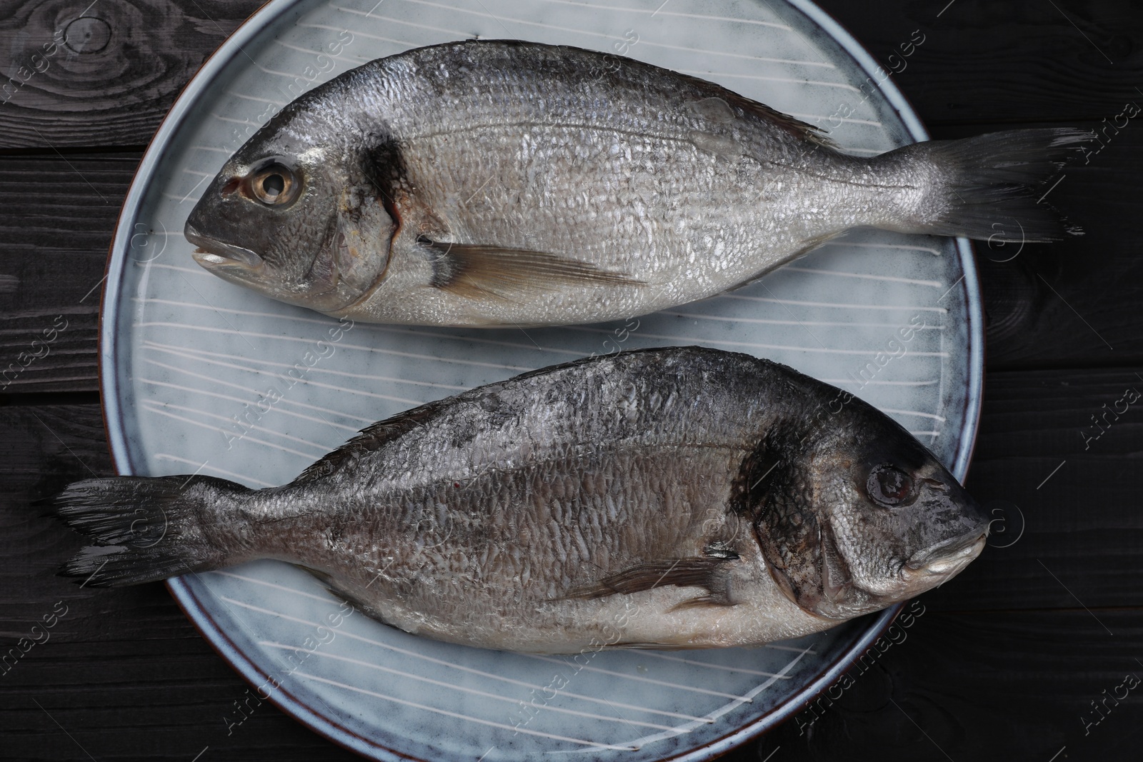 Photo of Fresh raw dorado fish on black wooden table, top view