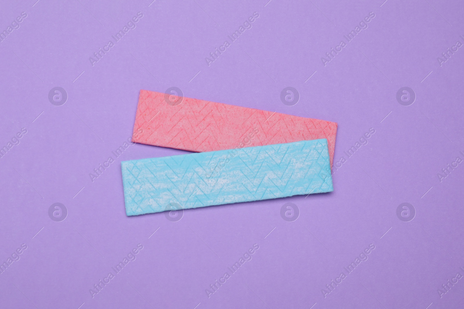 Photo of Sticks of tasty chewing gum on violet background, flat lay