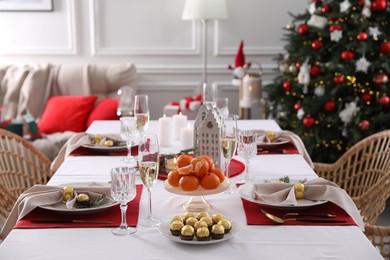 Photo of Christmas table setting with tangerines, candies and dishware indoors