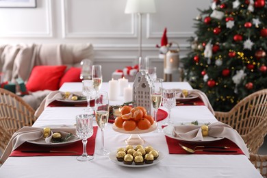 Christmas table setting with tangerines, candies and dishware indoors