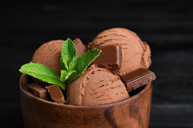 Photo of Wooden bowl of chocolate ice cream and mint on dark background, closeup