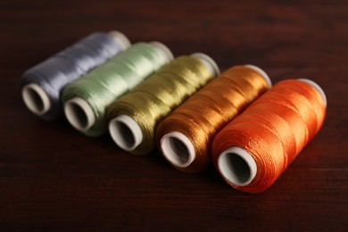 Photo of Set of color sewing threads on wooden table, closeup