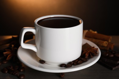 Photo of Cup of delicious hot chocolate, spices and coffee beans on wooden table