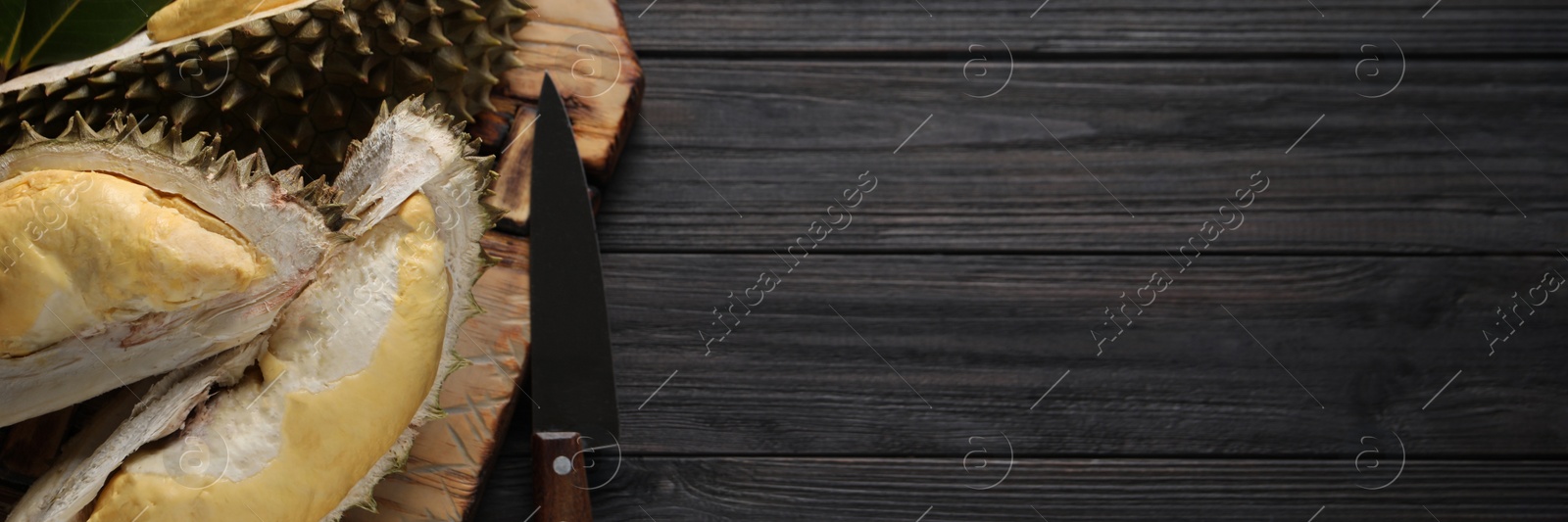 Image of Pieces of fresh ripe durian and knife on black wooden table, top view with space for text. Banner design