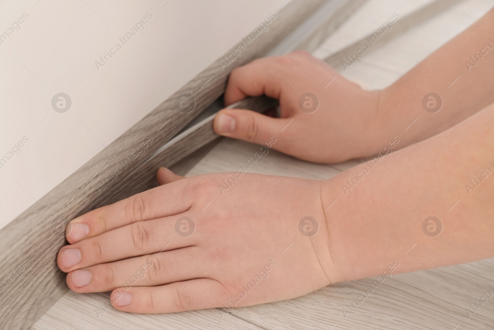 Photo of Man installing plinth on laminated floor in room, closeup