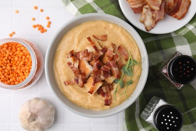 Photo of Delicious lentil soup with bacon and other ingredients on white tiled table, top view