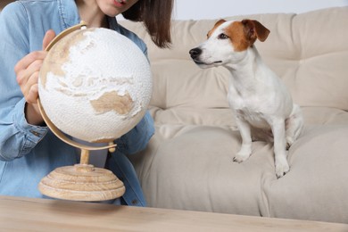 Woman with globe near dog indoors, closeup. Travel with pet concept