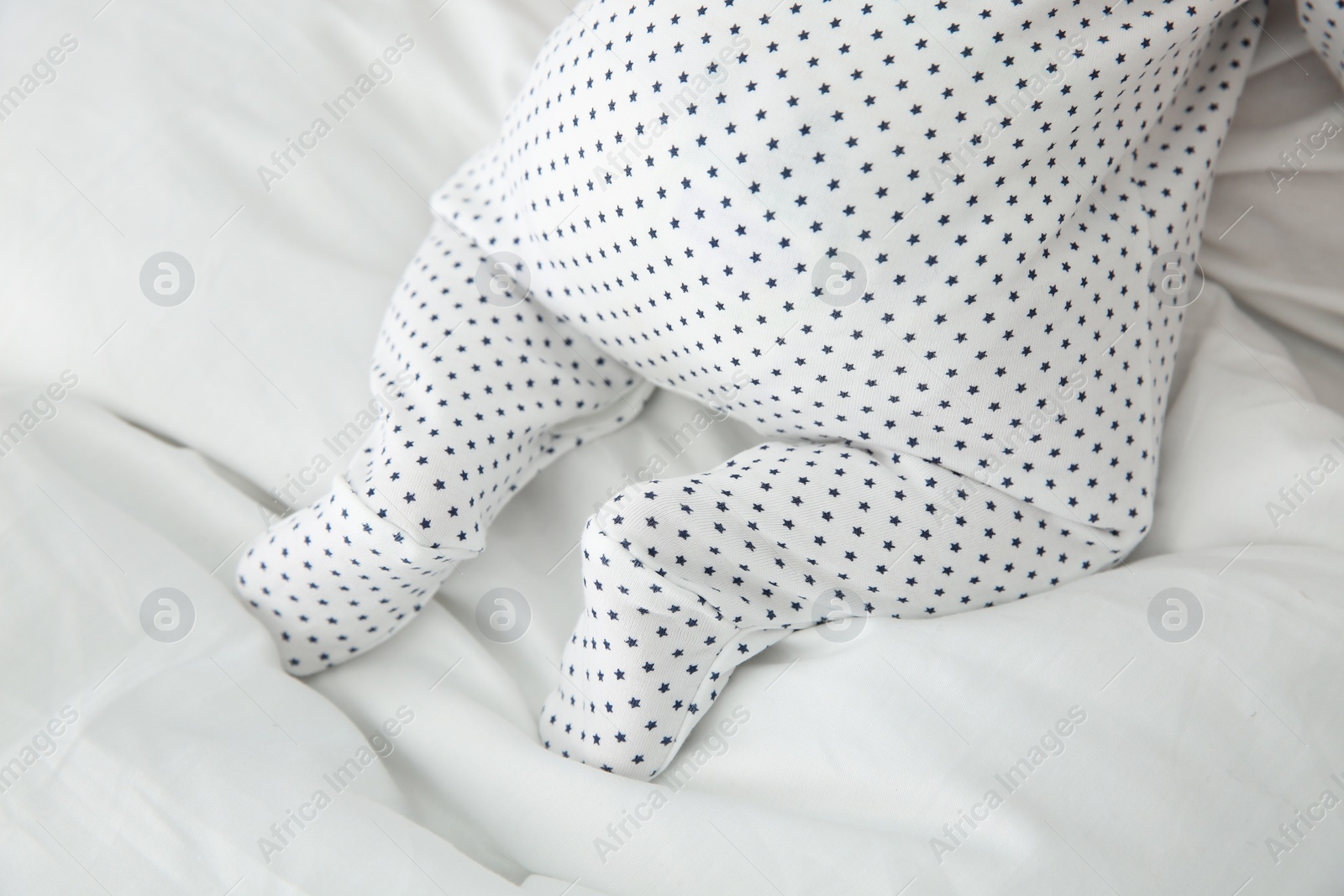 Photo of Adorable baby in cute footie on white sheet, closeup
