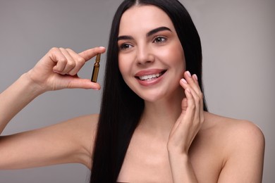 Photo of Beautiful young woman holding skincare ampoule on grey background