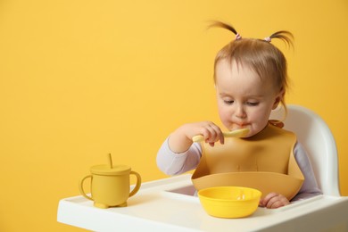 Photo of Cute little baby wearing bib while eating on yellow background