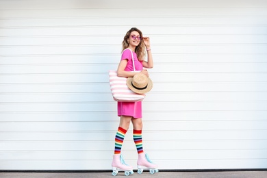 Happy young woman with retro roller skates near white garage door