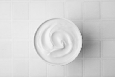 Photo of Delicious natural yogurt in bowl on white tiled table, top view