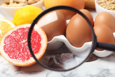 Photo of Different products with magnifier focused on eggs and grapefruit, closeup. Food allergy concept