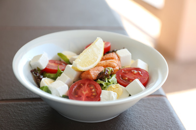 Delicious salad with salmon and feta cheese in bowl on table