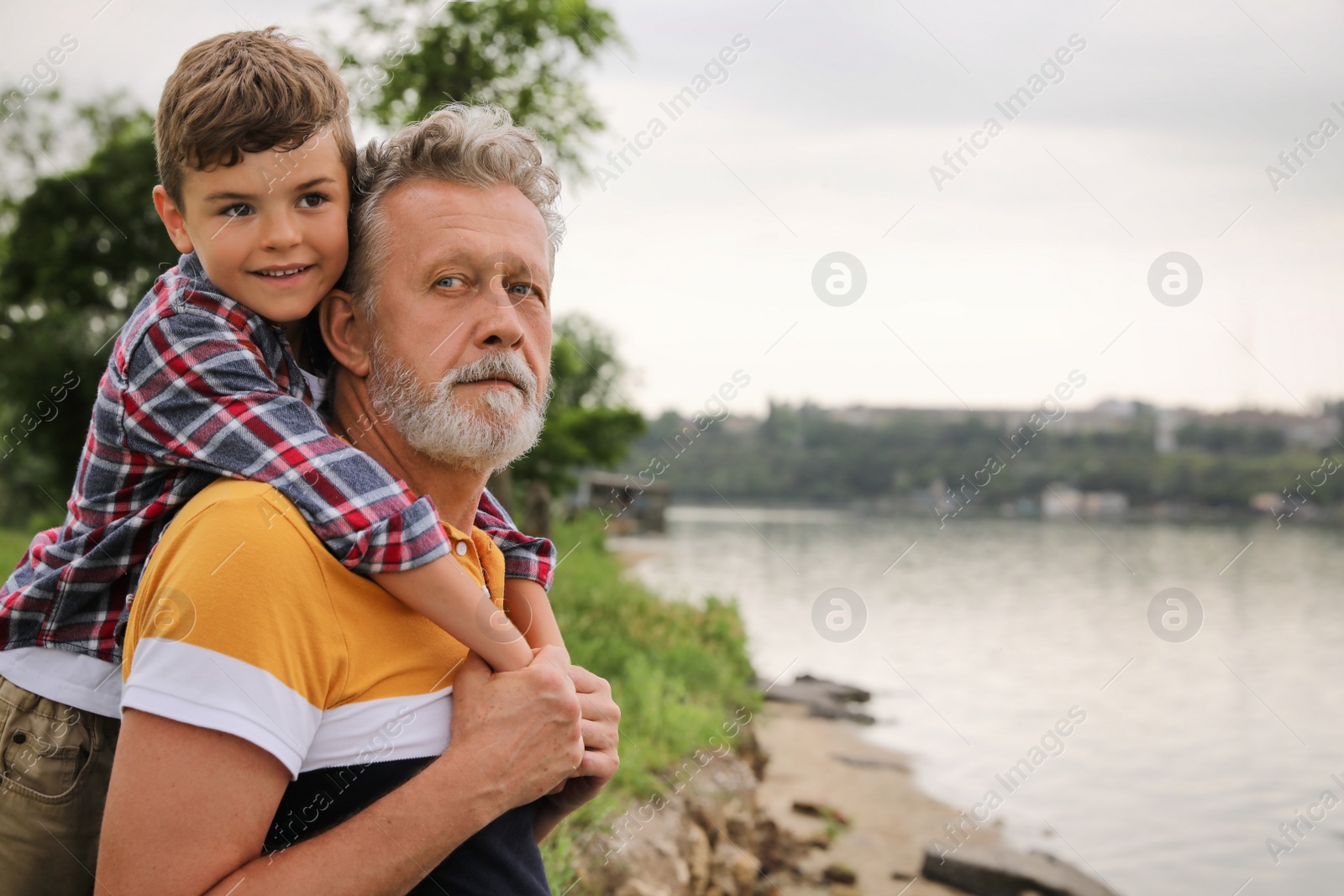 Photo of Cute little boy and grandfather spending time together near river, space for text