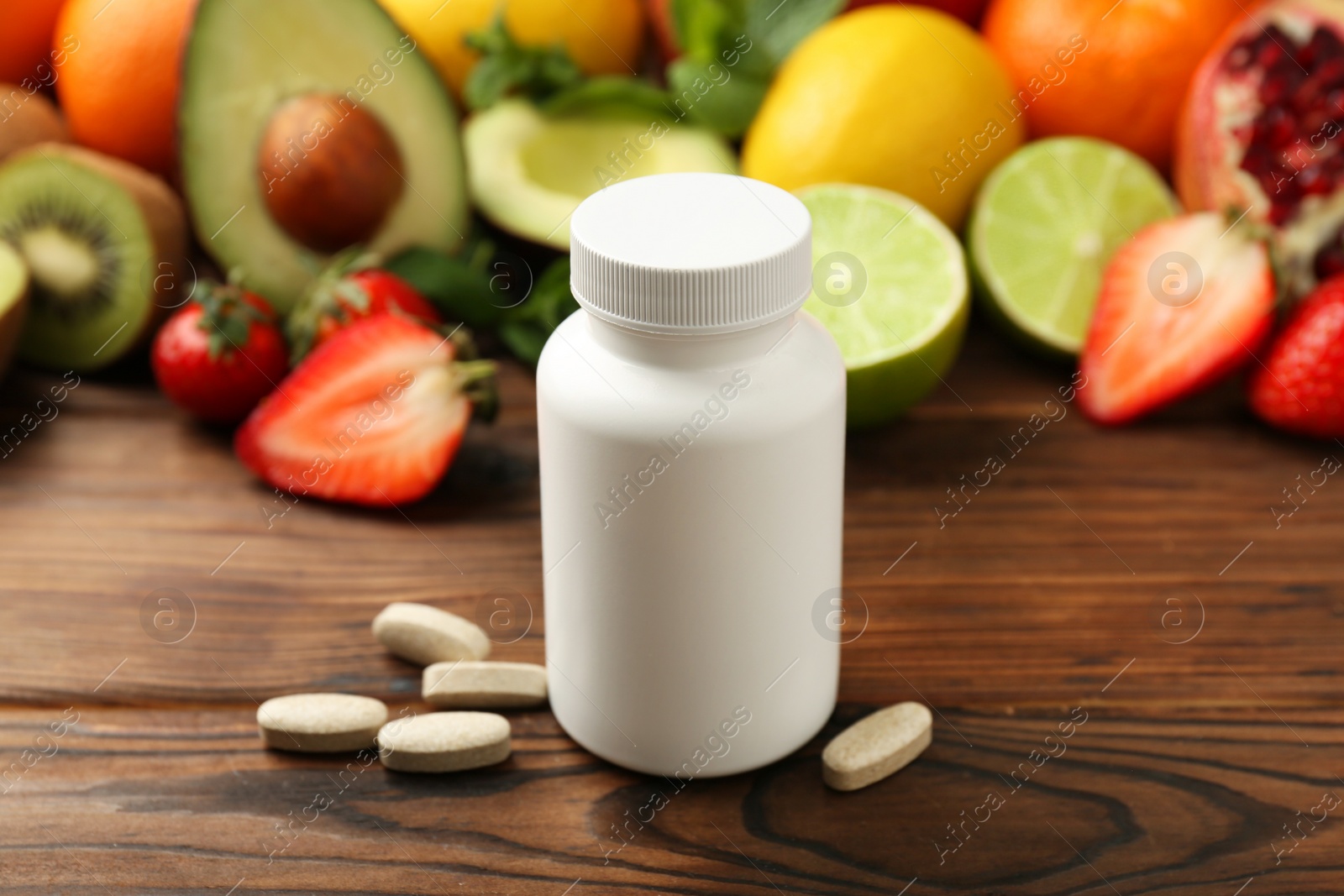 Photo of Vitamin pills, bottle and fresh fruits on wooden table