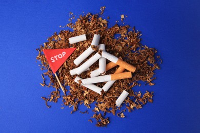 Photo of Broken cigarettes, red flag with word Stop and tobacco on blue background, flat lay. Quitting smoking concept