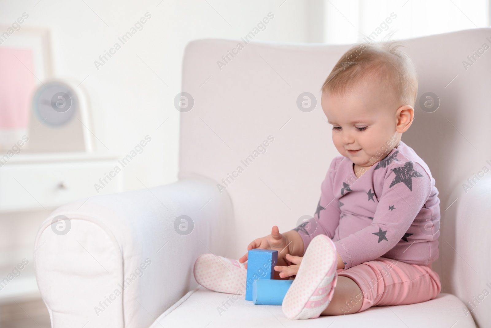 Photo of Cute baby girl playing with building blocks in armchair at home. Space for text
