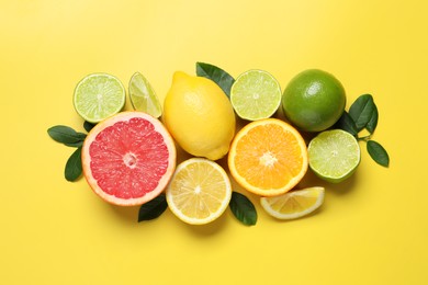 Photo of Different cut and whole citrus fruits on yellow table, flat lay