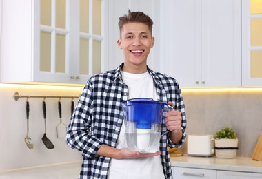 Photo of Happy man with water filter jug in kitchen