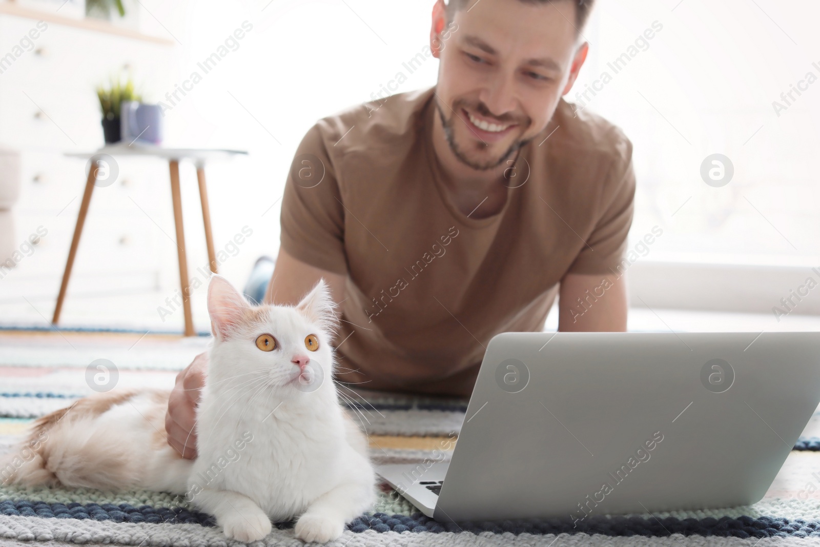 Photo of Young man with cute cat and laptop at home