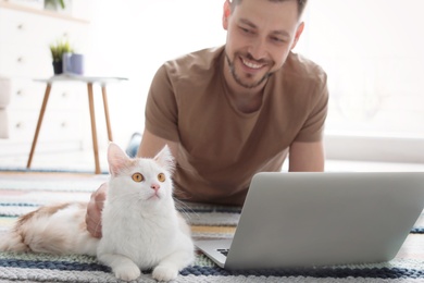 Young man with cute cat and laptop at home